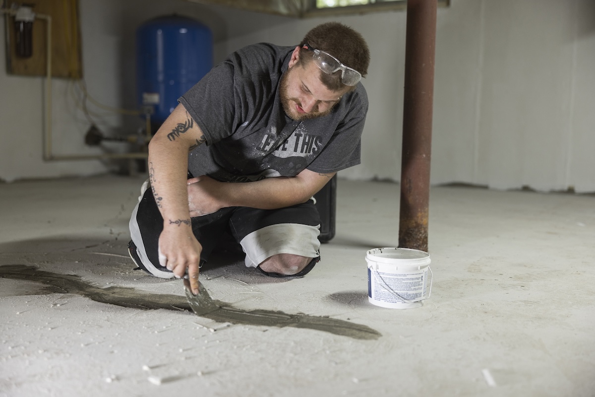 A homeowner filling a crack in a basement floor with all-purpose putty.