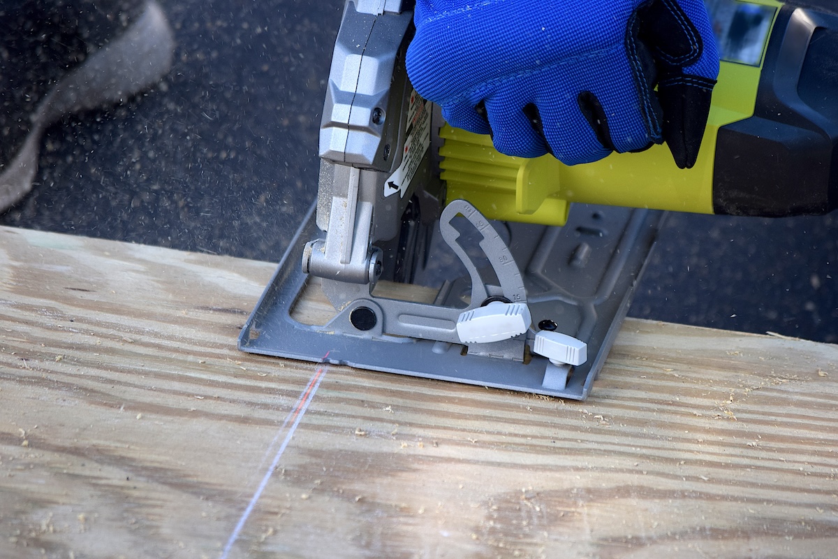 A person using a circular saw to cut a sheet of plywood outdoors.