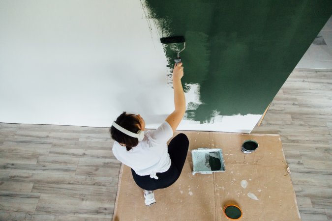 A DIYer painting a room green.