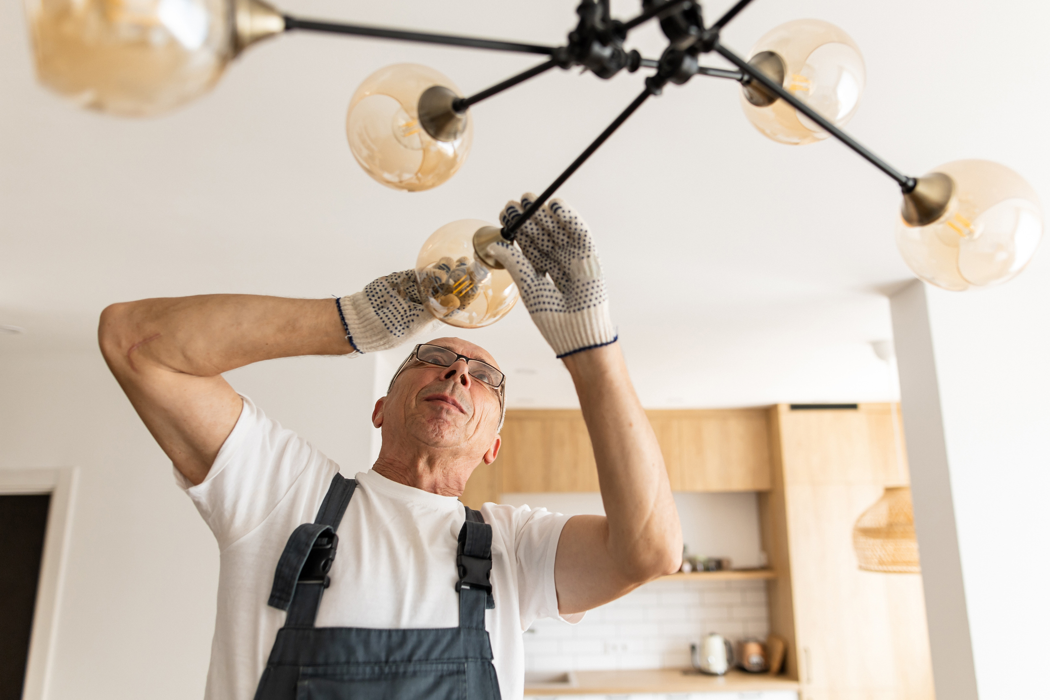 Older man hanging a ceiling light fixture.