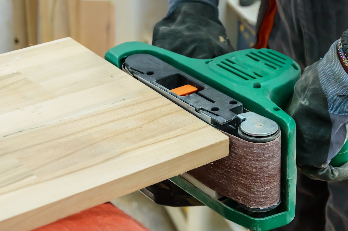 A DIYer using a belt sander to remove wood from the end of a board.