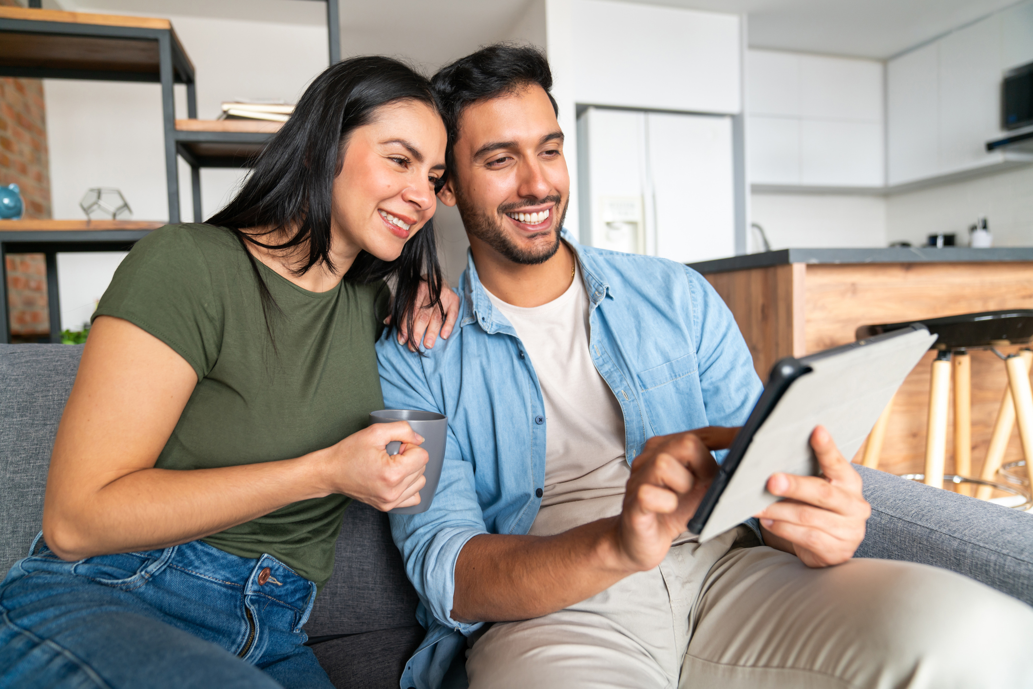 Happy couple sitting on couch at home enjoying pictures on an iPad.