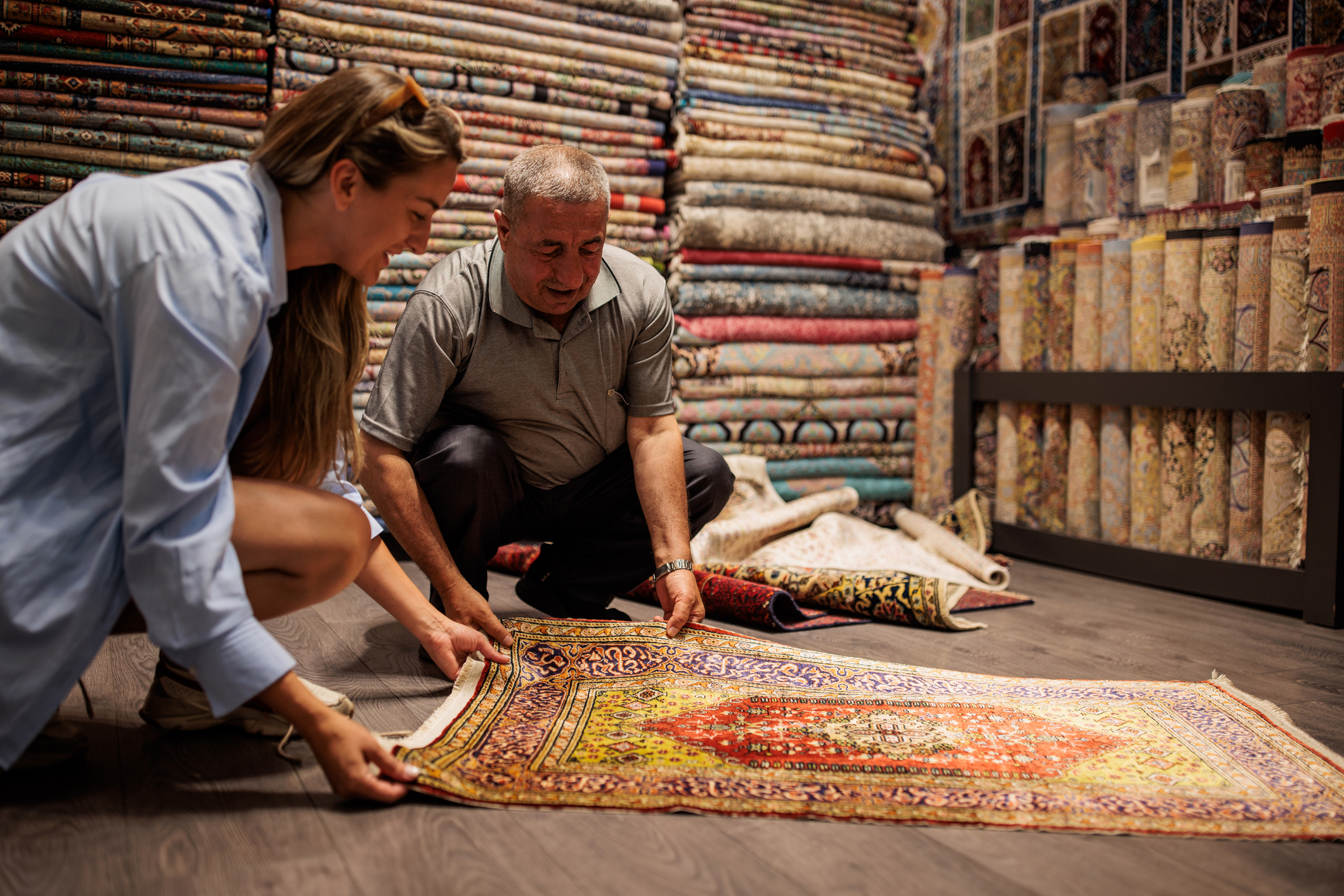 Male store owner showing vintage rugs to a woman customer.