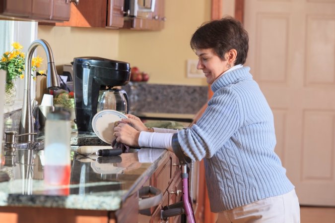 A homeowner with walking canes washing dishes at the kitchen sink.