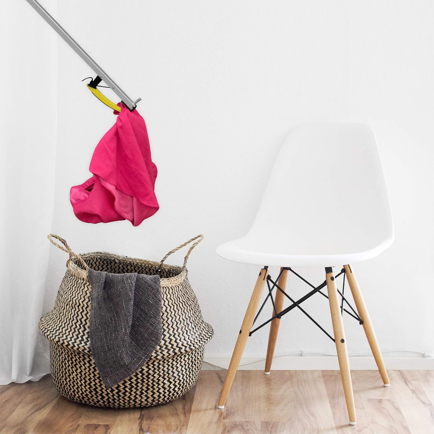 A person using a grabber tool to pick up laundry and place it in a hamper.