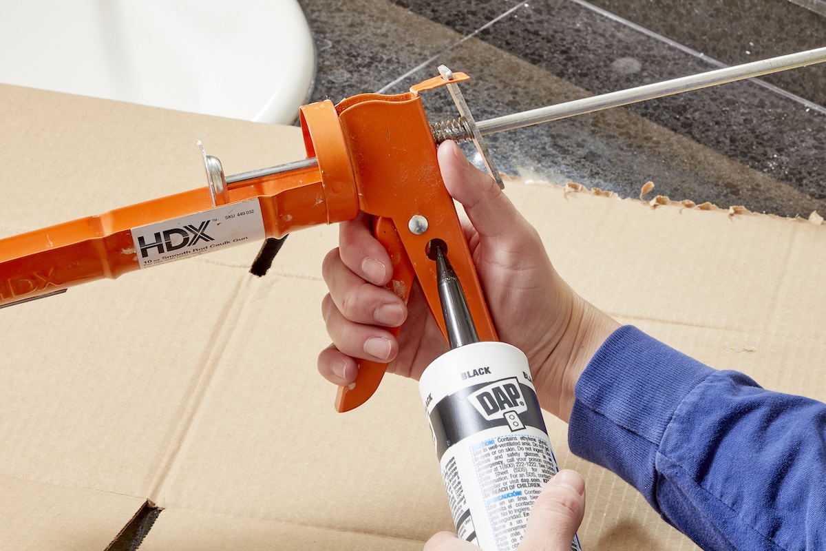 A DIYer loading a caulking gun and cutting the tip of the caulk tube.