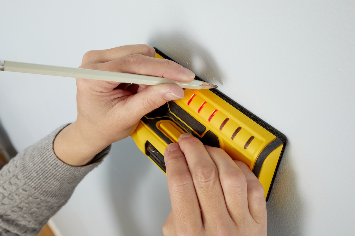 A DIYer using a stud finder to find wall studs.