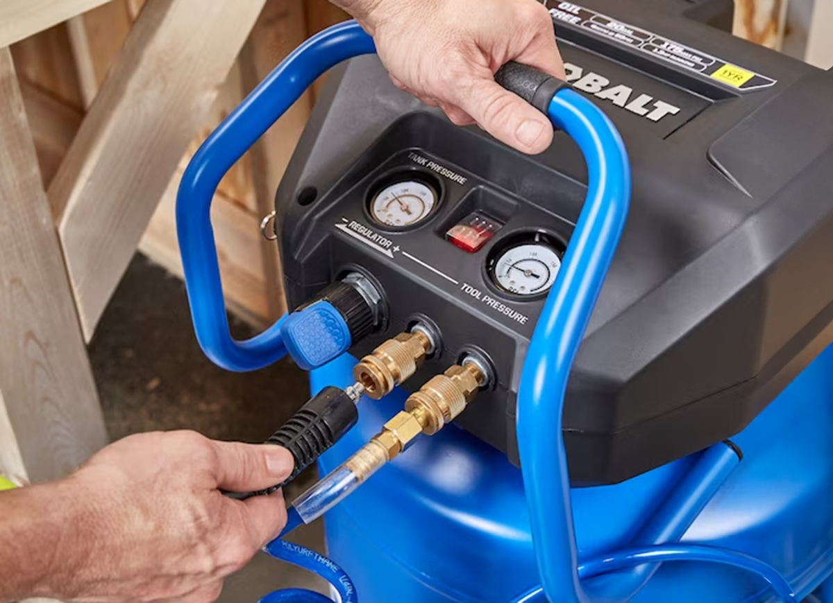 A person using an air compressor to use pneumatic tools in a home workshop.