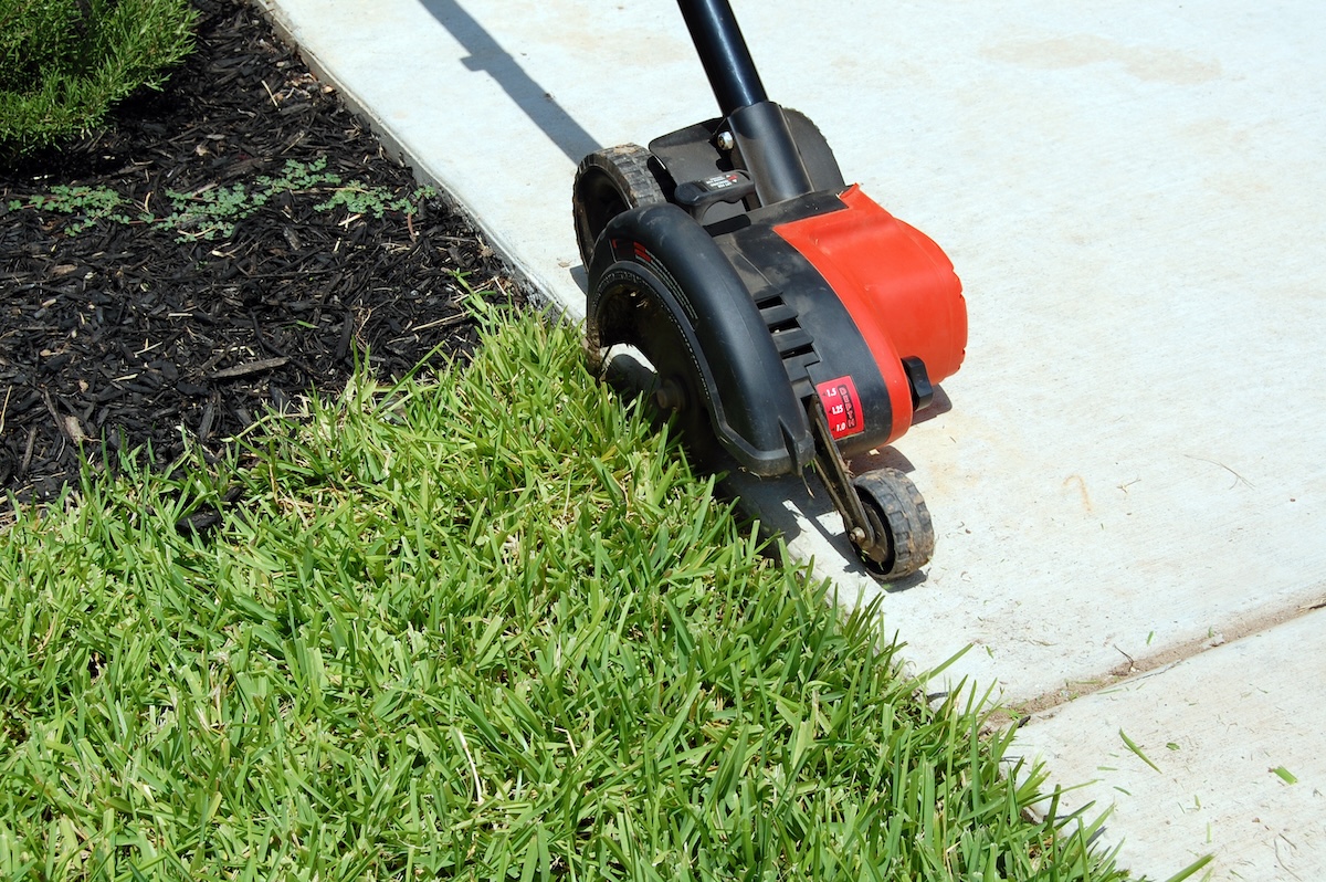 A red lawn edger moving along line between grass and cement walkway.