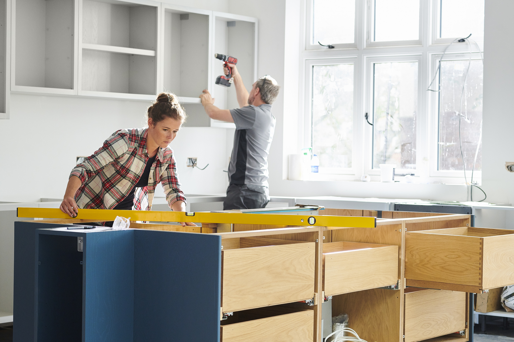 Man and woman installing cabinets and drawers in a kitchen.