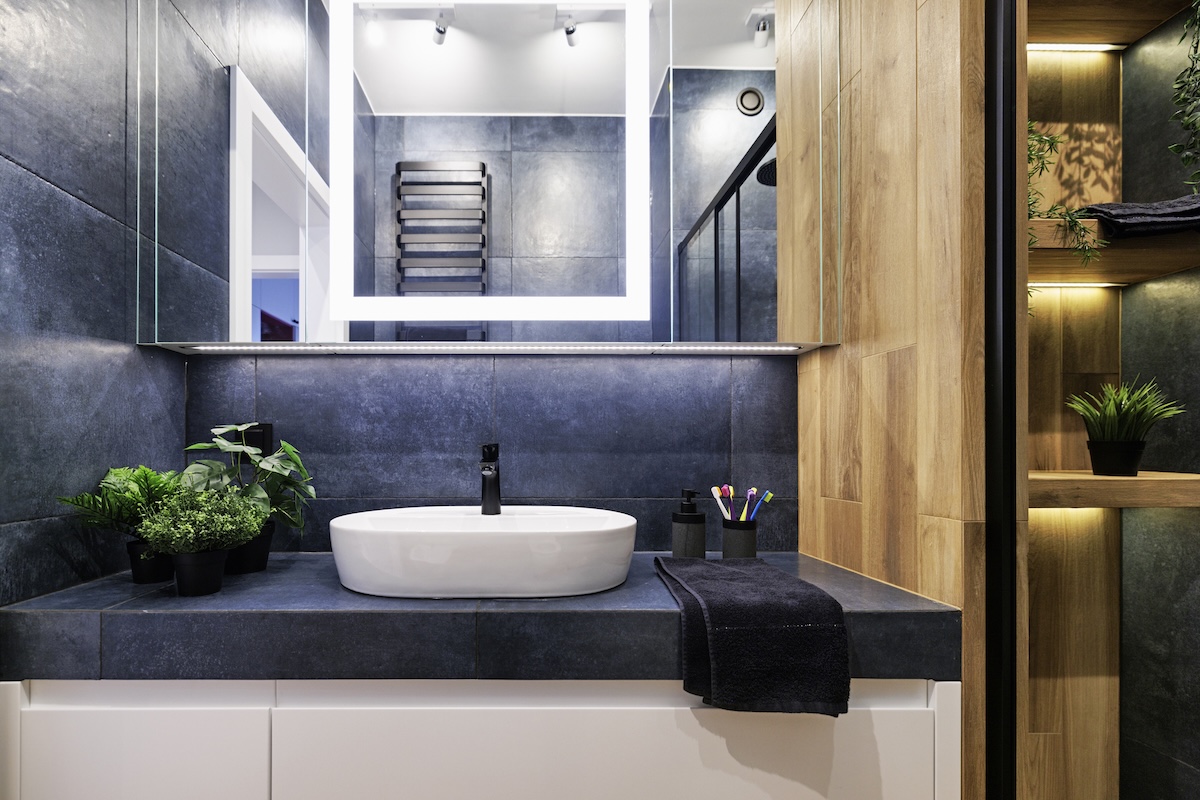 A dark blue tiled bathroom countertop with sink and mirror.