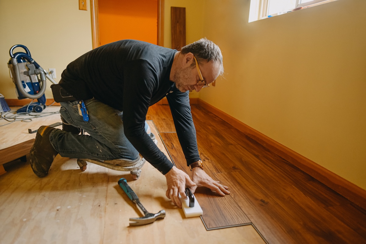 A DIYer installing vinyl plank flooring in his house.