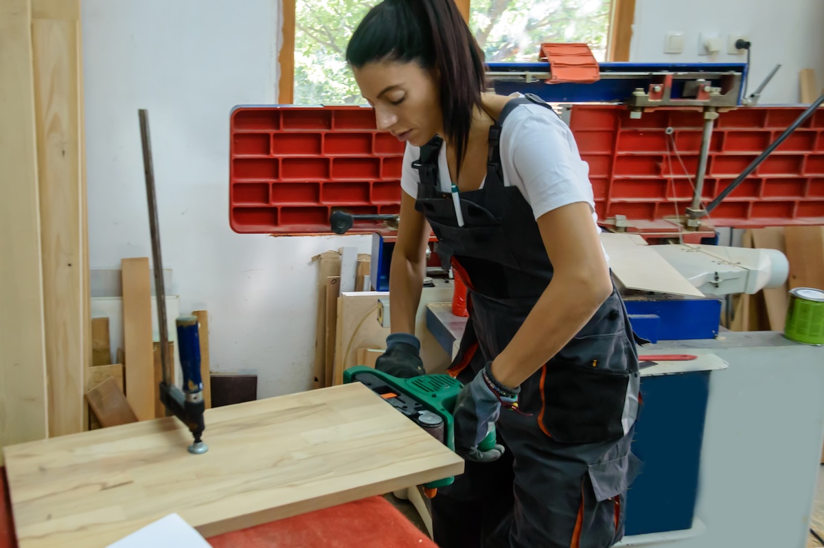 A DIYer using a belt sander to smooth a wood board.