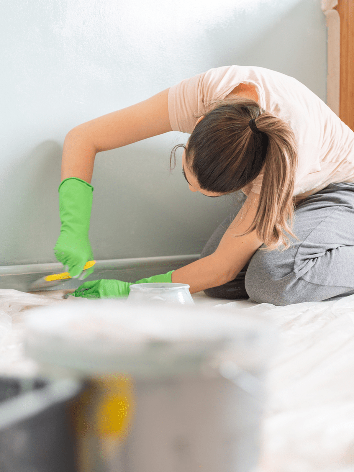 A DIYer painting baseboards in a carpeted room.