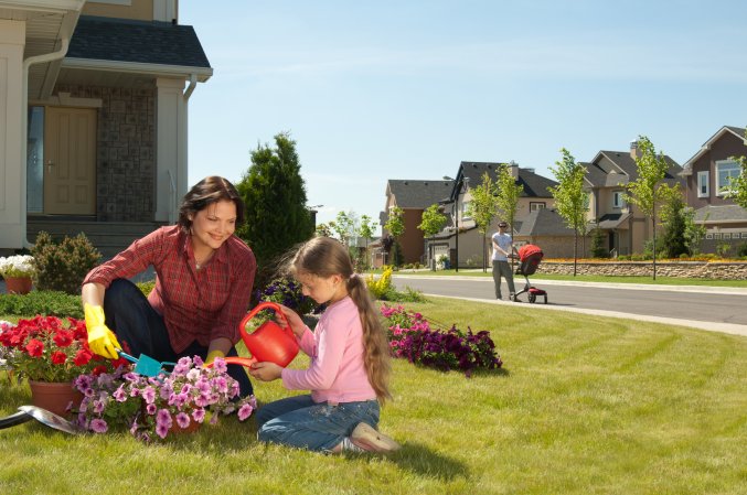 Mother and daughter having gardening time outside on the front yard of their suburban house in the Spring.