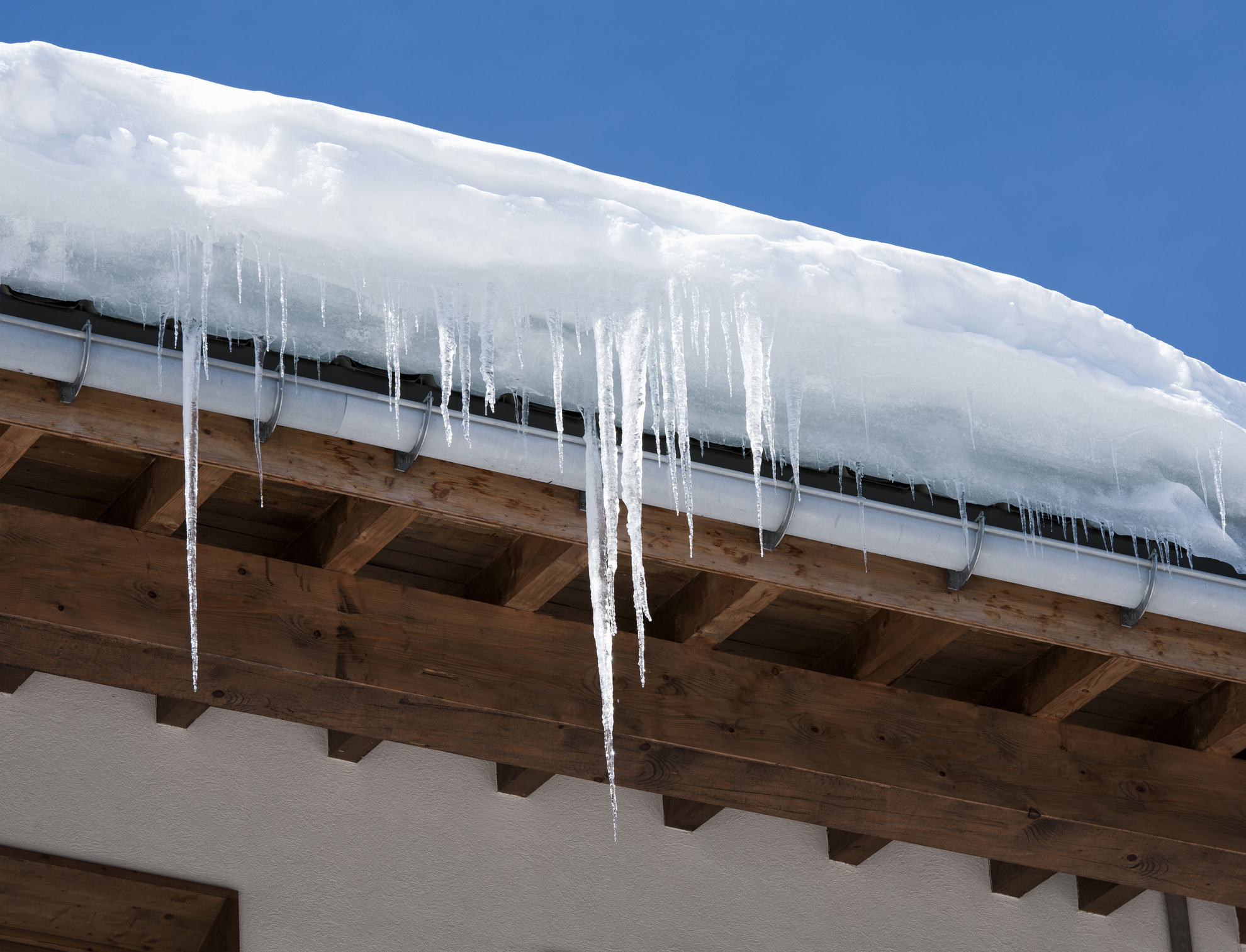 Long icicles and snow overhaning the roof and gutter of a home.