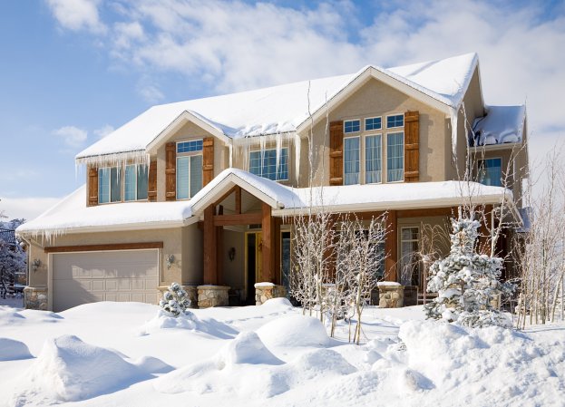 A snow covered tan home with icicles hanging down.