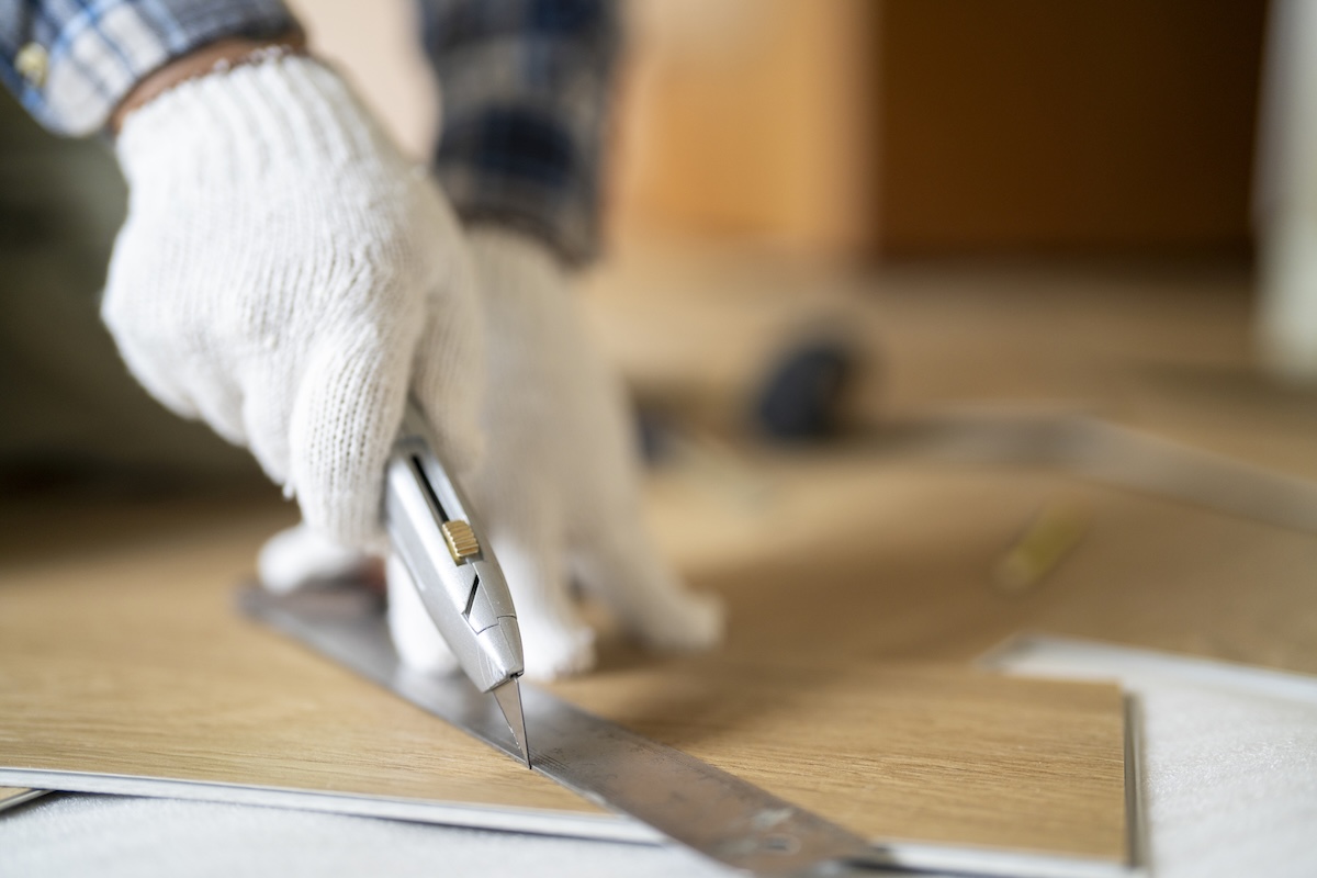 A DIYer cutting a plank of luxury vinyl flooring during installation.