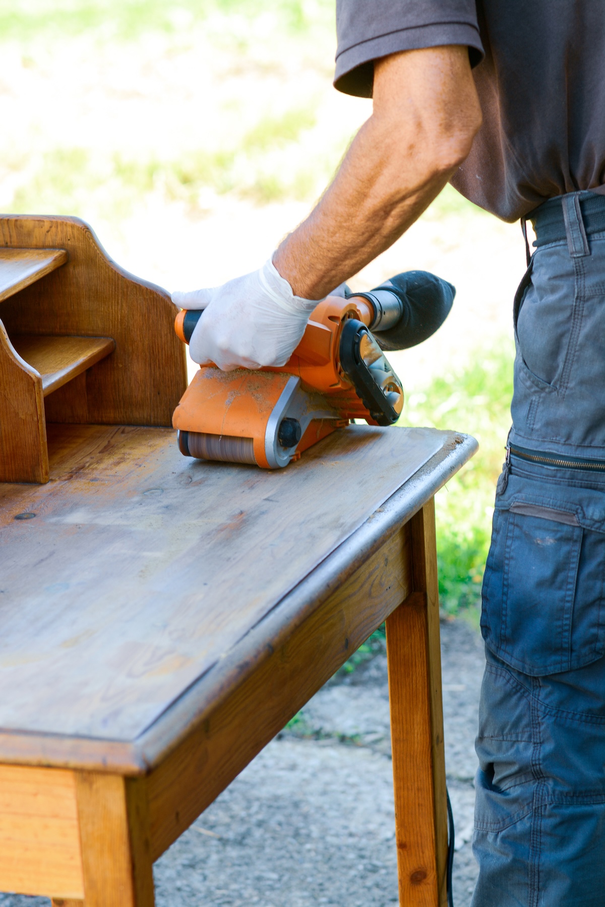 A DIYer using a belt sander to remove stain from an old desk.