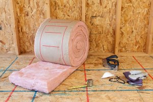 A roll of insulation and tools by an open wall.