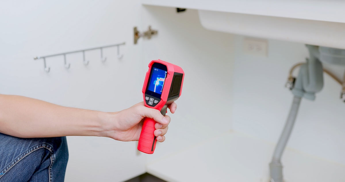 A person using a thermal camera to identify leaks under a sink.