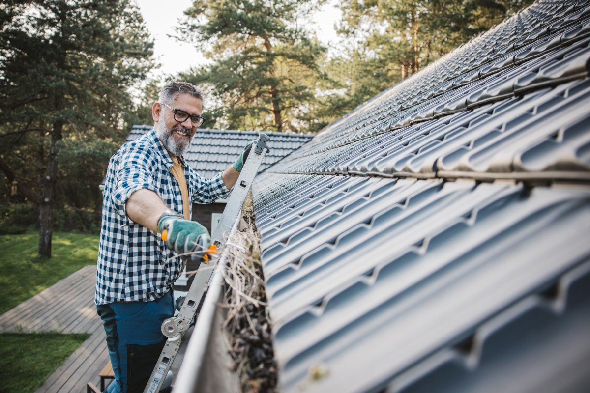 Man cleaning leaves from gutters of house.