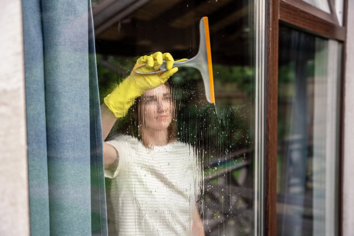 A woman cleaning window glass of house with a squeegee.