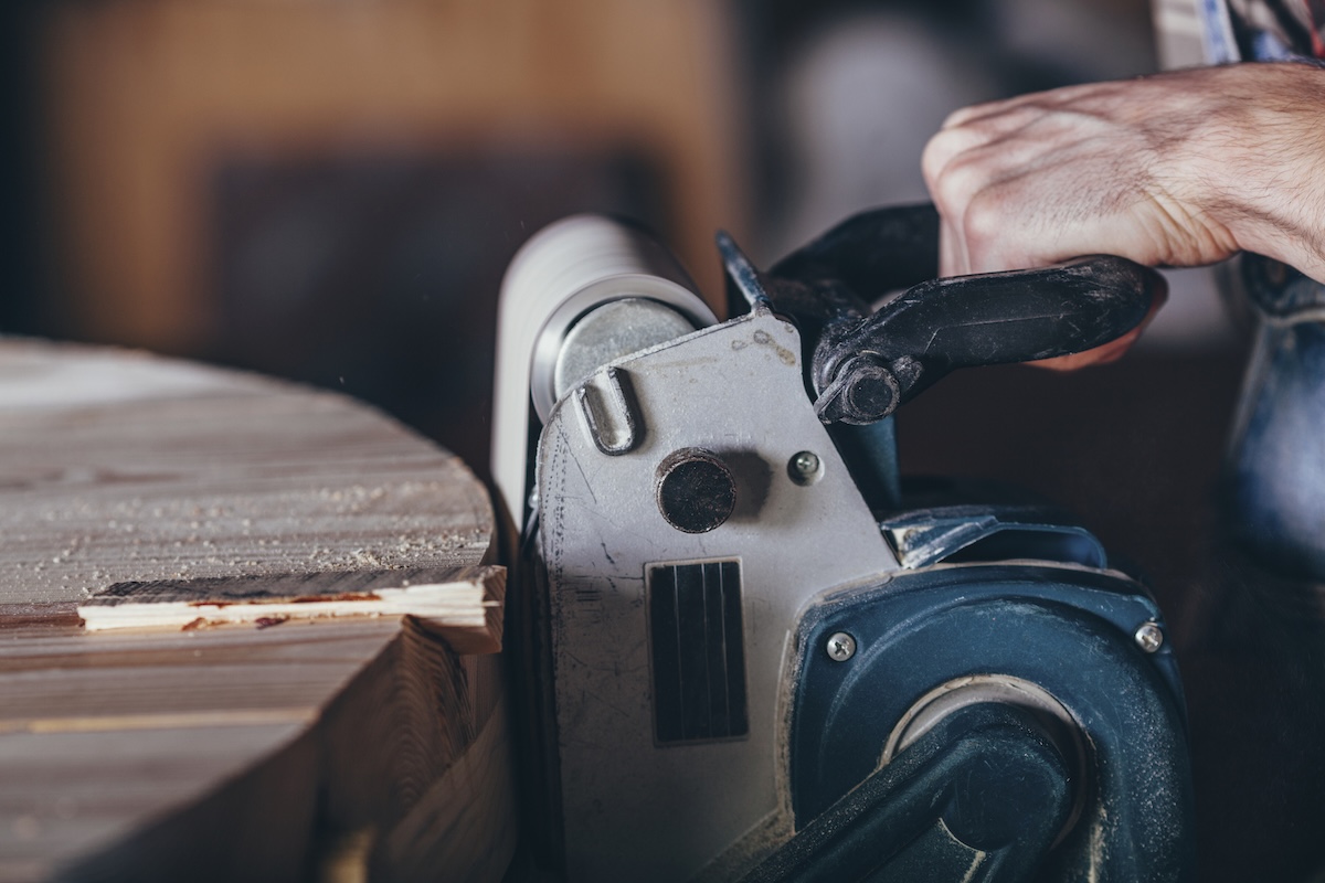 A person using a belt sander on a rough wood table.