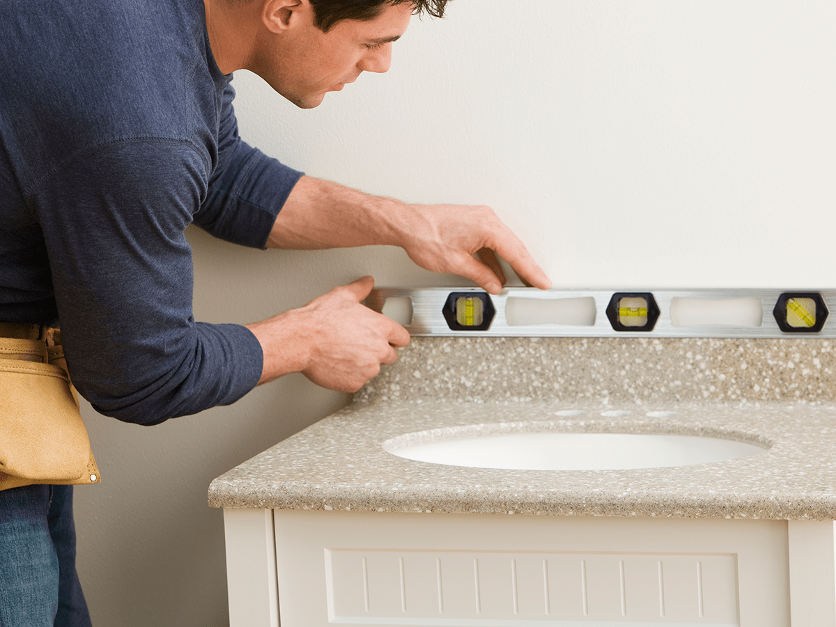 A DIYer using a level when installing a new bathroom countertop.