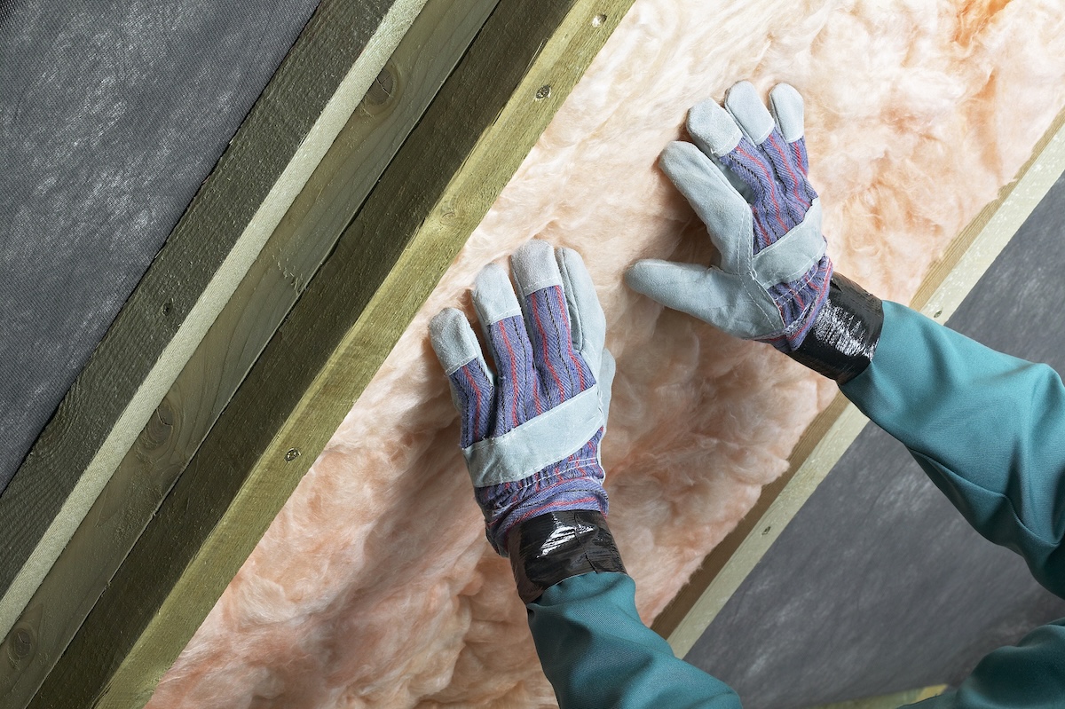 A person installing insulation between wall studs.