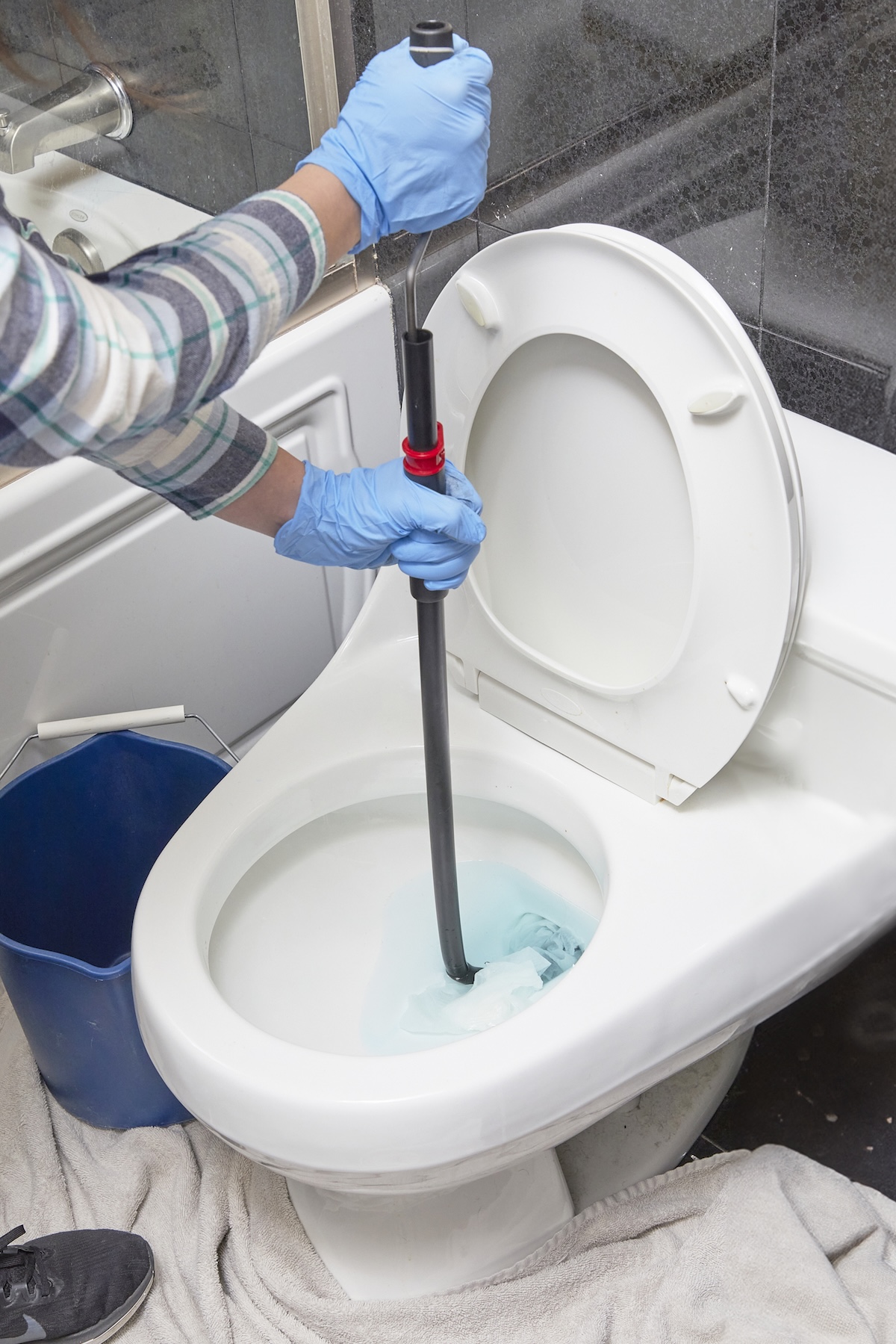 A DIYer using a drain snake or auger to unclog a toilet.