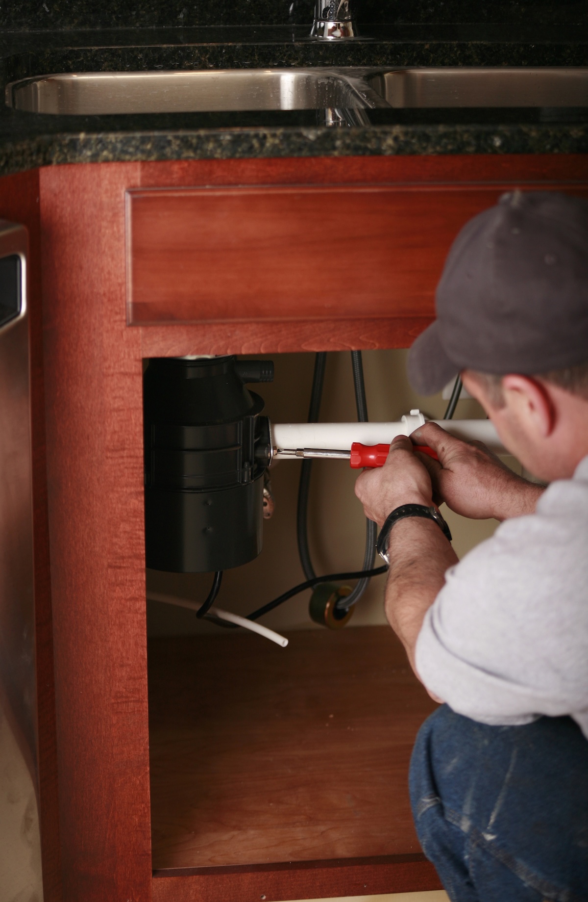 A DIYer working to fix a clogged garbage disposal under a kitchen sink.