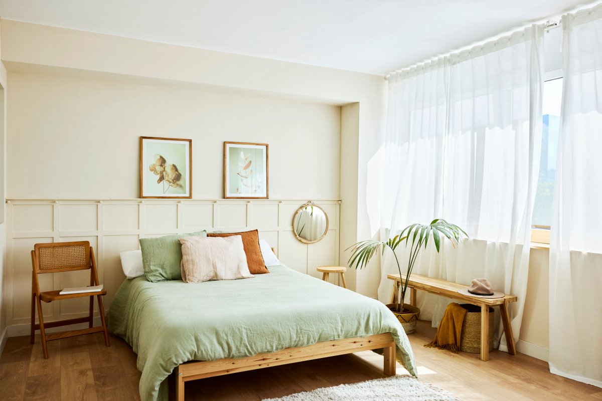 Modern tidy bedroom with sage green bedspread and light wood furniture.