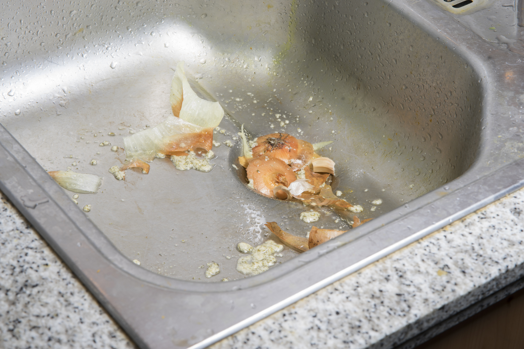 Messy stainless steel kitchen sink with food scraps