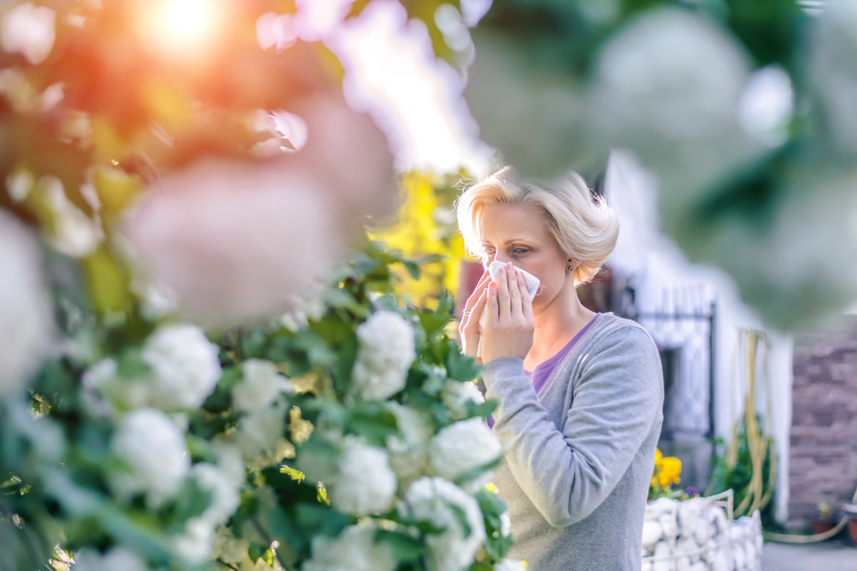 Older woman sneezing into a tissue outside by flowers