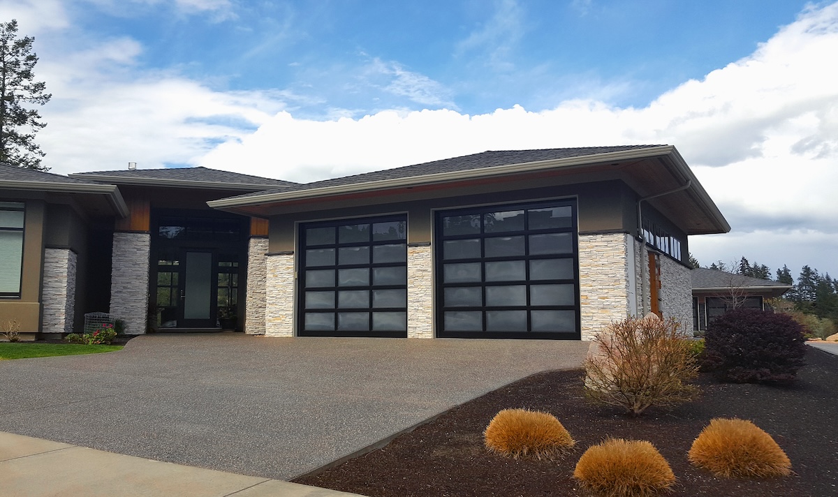 A modern home with light stonework and garage doors with glass panels.