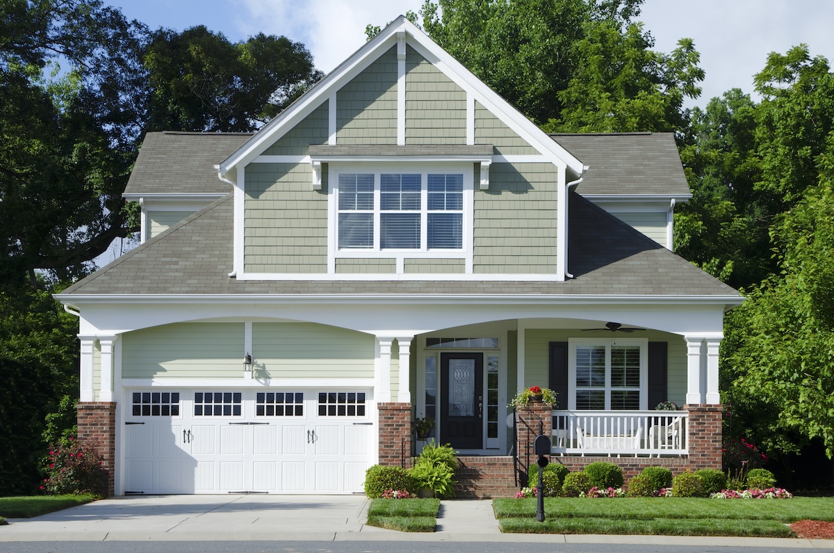 A green cottage-style home with white trim and white garage doors.