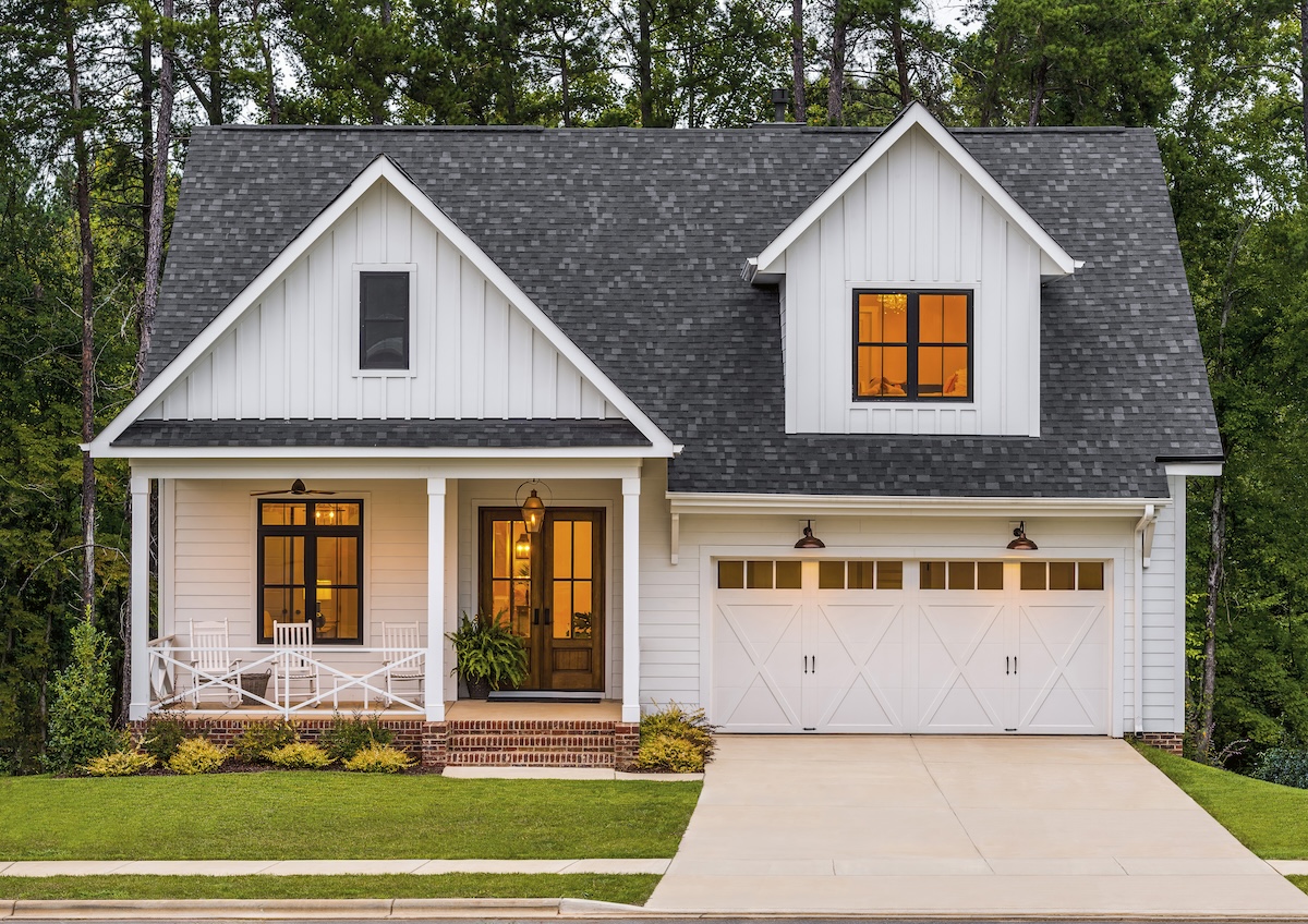 A white farmhouse style home with lit garage doors.